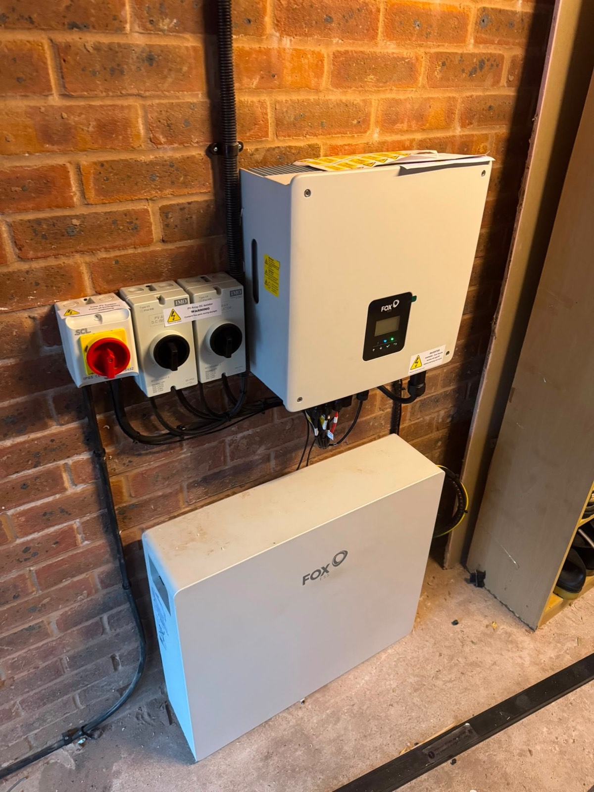 Fox ESS inverter and battery storage unit wall-mounted on brickwork with isolators and conduit run neatly alongside