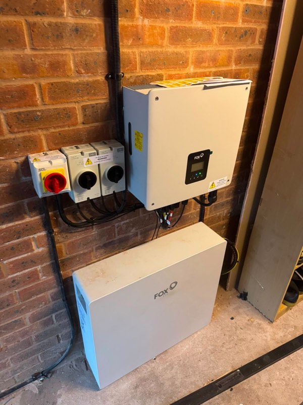 Fox ESS inverter and battery storage wall-mounted on brickwork with isolators and neat conduit